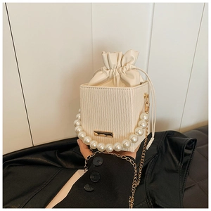 Detail of beige pleated crossbody bag featuring pearl handle and gold chain strap
