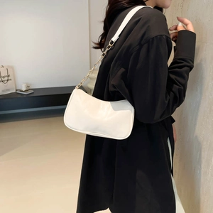 Chic white curved underarm bag with gold chain strap worn by a model in modern interior