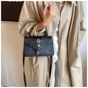 Détail d'un sac bandoulière noir géométrique avec boucle dorée porté par un mannequin en trench