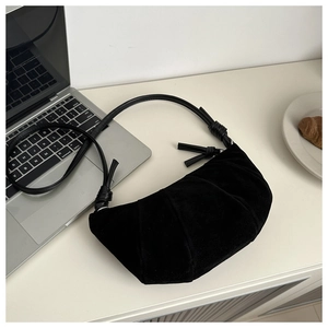 Detail of black pleated croissant shoulder bag with decorative knots on a white desk