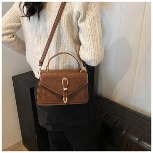 Gros plan sur sac bandoulière marron rétro avec boucle dorée en U et texture cousue