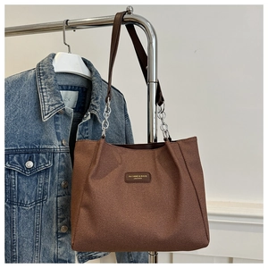 Close-up of brown textured canvas tote bag with leather handles and silver chain detail