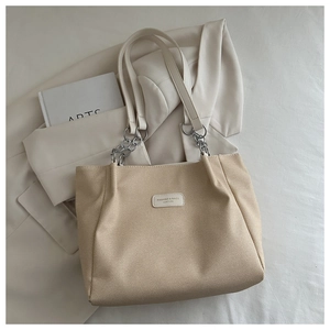 Detailed shot of beige woven tote bag with silver chain handle and minimalist texture