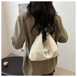 Detail of white leather shoulder bag featuring a silver metal butterfly and chain strap