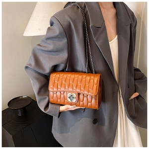 Detail of a brown quilted chain bag featuring a floral metal clasp and pleated texture