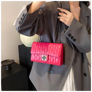 Detail of rose red quilted chain bag featuring a decorative metal flower clasp and leather texture