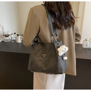 Detail of black matte tote bag featuring a plush white cloud charm and metal logo patch