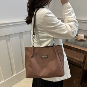 Brown woven tote bag with chain strap shown on model for stylish daily commuting use