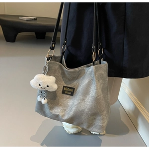Detail of grey tote bag with matte texture, black straps, and white cloud plush charm