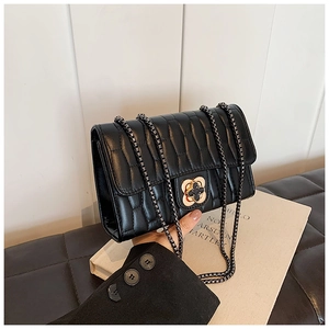 Detail of black pleated crossbody bag with a clover-shaped gold rotating metal lock clasp