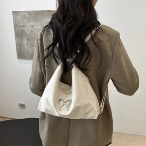 White glossy butterfly hobo bag worn by model in a minimalist indoor setting