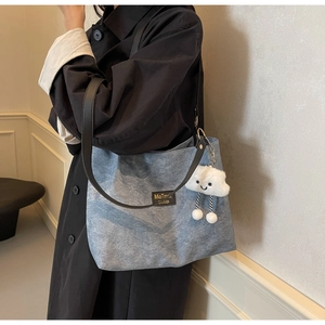 Detail of blue denim tote bag with black leather straps and a white cloud plush charm