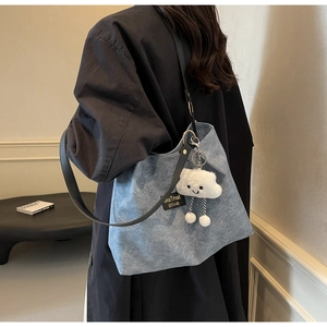 Detail view of denim tote bag with black leather strap and cloud-shaped plush pendant