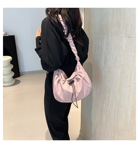 Detailed view of pink pleated crossbody bag worn by model in a modern indoor setting