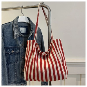Detailed view of red and white striped canvas tote bag hanging on a hanger next to denim jacket