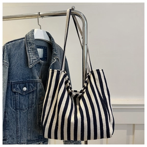 Detail of a large striped canvas tote bag hanging next to a blue denim jacket