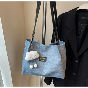 Close-up of light blue denim tote bag with white cloud plush pendant and leather brand tag