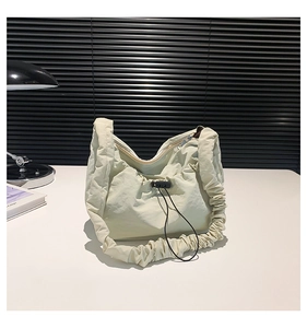 Detail of cream drawstring tote bag with pleated strap and zipper on white table