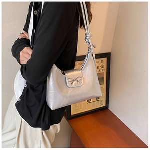 Silver metallic tote bag with knot shoulder strap and bow detail on wooden table