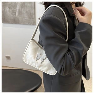 Detail of cream baguette bag with silver butterfly buckle on a model in a grey suit