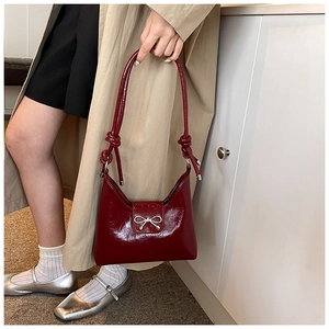 Detail of dark red glossy shoulder bag featuring silver metal bow and knotted strap design
