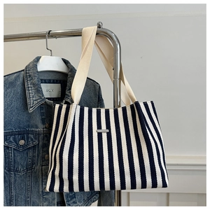 Détail d'un sac cabas en toile à rayures noires et blanches avec plaque logo métallique