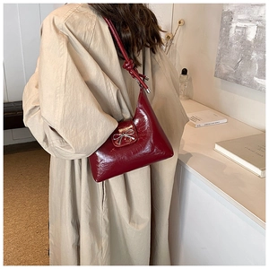 Detail of burgundy glossy shoulder bag featuring a silver bow buckle and knotted strap