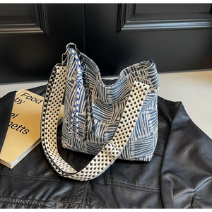 Close-up of blue textured woven tote bag with a checkered strap and tassel details