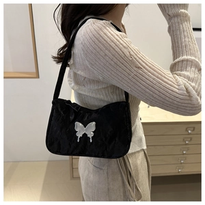 Detail of black textured shoulder bag with a silver butterfly ornament on model
