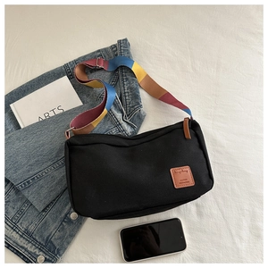 Detail of black canvas messenger bag with a colorful striped strap and leather logo patch