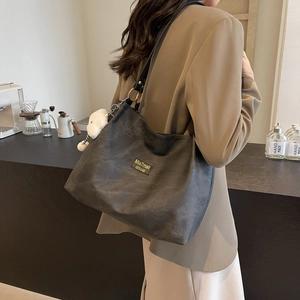 Large dark grey tote bag with chain pendant shown on model in a modern setting