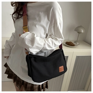 Detail of black canvas messenger bag with colorful strap and leather logo patch