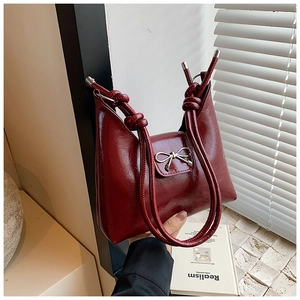 Detail of burgundy tote bag featuring a silver metal bow and unique knotted handles