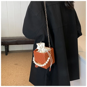 Detail of orange plaid box bag with pearl handle and metal chain on black coat