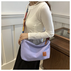Detail of lavender canvas crossbody bag with colorful striped wide strap and leather logo