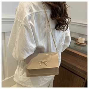 Modèle portant un sac bandoulière beige avec boucle nœud dorée et bandoulière chaîne