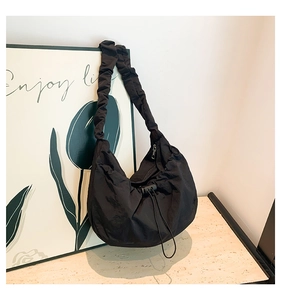 Detailed view of black pleated nylon cloud bag with ruched strap on stone surface