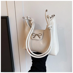 Close-up of white glossy patent leather bag with silver bow buckle and rope knot handle