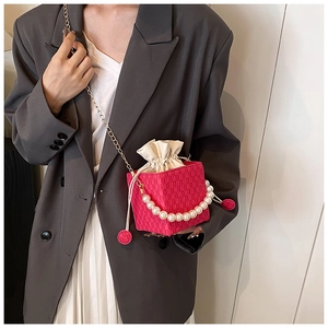 Detail of rose red woven bucket bag featuring large pearl handle and gold chain strap