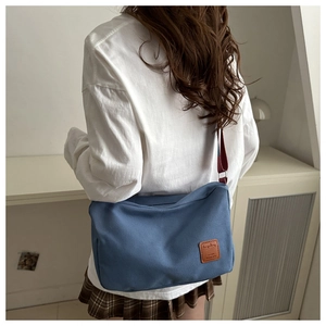 Detailed view of the blue canvas messenger bag featuring a leather logo patch and strap