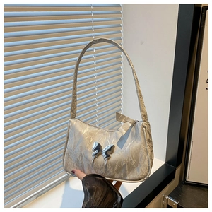 Macro detail of Y2K silver butterfly accent on metallic pleated shoulder bag for women