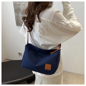 Detail view of navy blue canvas crossbody bag with leather patch on a model back