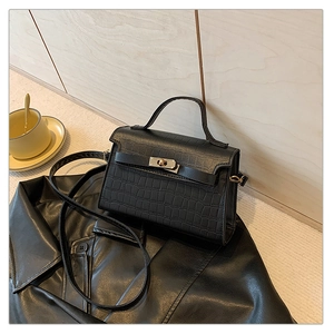 Detail of black crocodile texture handbag with gold twist lock and leather shoulder strap