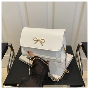 Détail d'un sac à bandoulière en cuir blanc avec boucle nœud doré et chaîne dorée