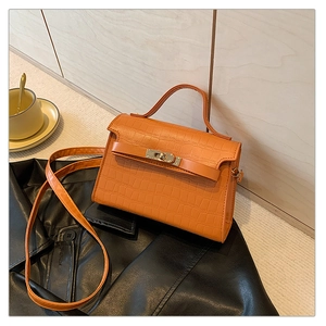 Detail shot of orange crocodile textured handbag with metallic twist-lock on a leather jacket