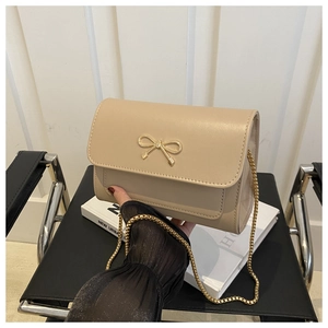 Détail du sac bandoulière beige avec fermoir nœud doré et bandoulière en chaîne chic