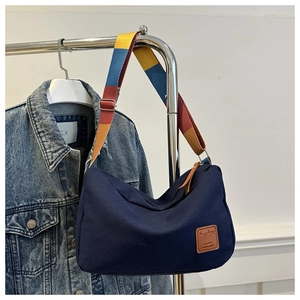 Detail of dark blue canvas bag with colorful striped strap and brown leather logo patch