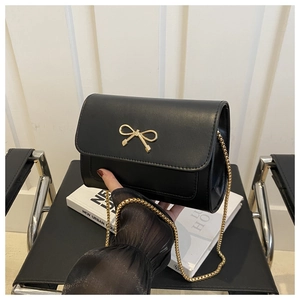 Détail d'un sac bandoulière noir avec boucle nœud dorée et fine bandoulière en chaîne