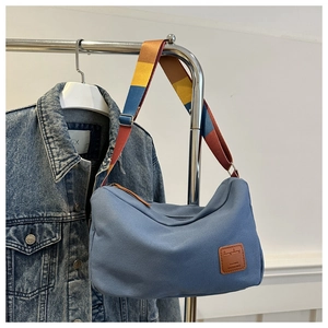 Detail of blue canvas bag with colorful woven shoulder strap and brown leather logo