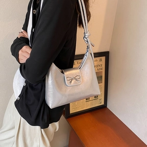 Silver metallic crossbody bag with bow detail and textured finish shown on a model